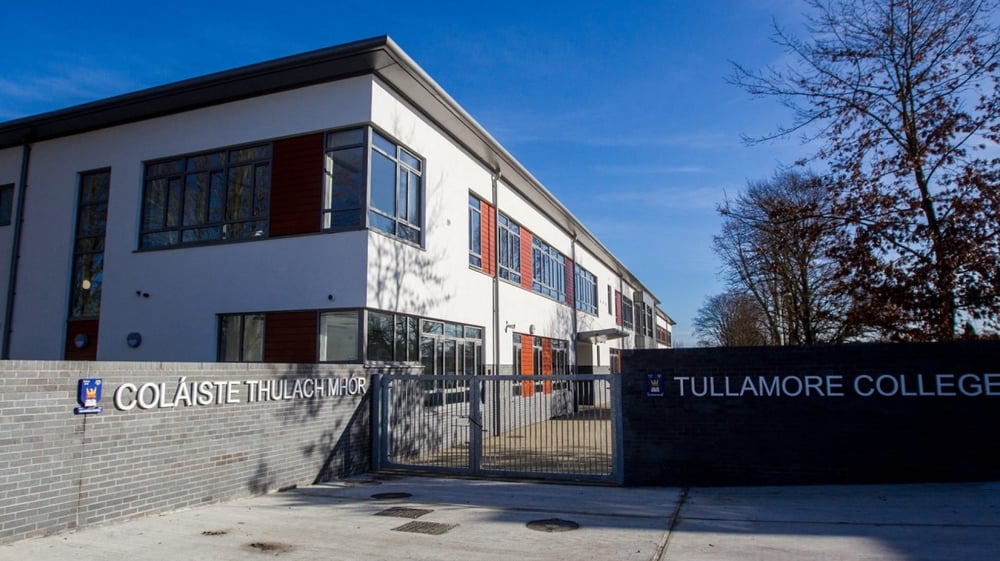 Das moderne Gebäude des Tullamore College mit großen Fenstern steht vor blauem Himmel und umgeben von Bäumen.