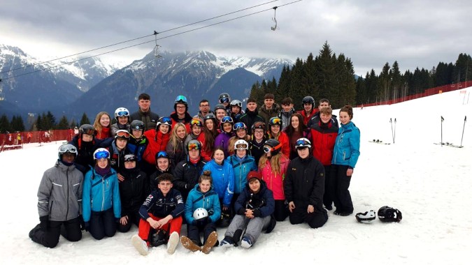Eine große Gruppe von Schülern des Tullamore College posiert zusammen in einer verschneiten Berglandschaft mit hohen Gipfeln im Hintergrund.