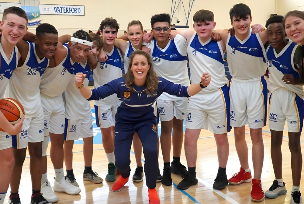 Eine Gruppe junger Basketballspielerinnen und -spieler des Tyndall College posiert in der Sporthalle in blauen und weißen Uniformen.