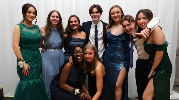 Eine Gruppe elegant gekleideter Personen posiert gemeinsam vor weißem Hintergrund auf dem Campus des Tyndall College.