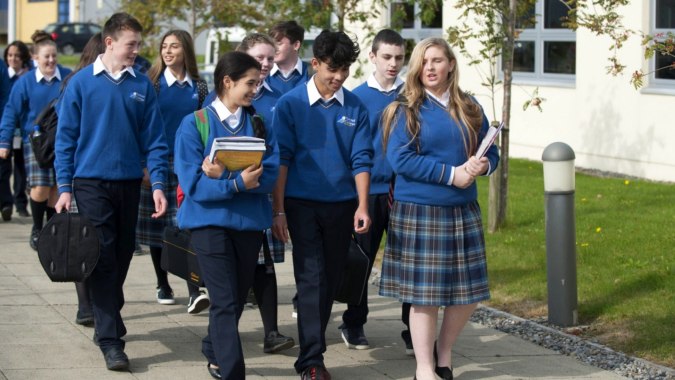 Eine Gruppe von Schülerinnen und Schülern in Schuluniformen geht auf einem Weg auf dem Campus des Tyndall College.