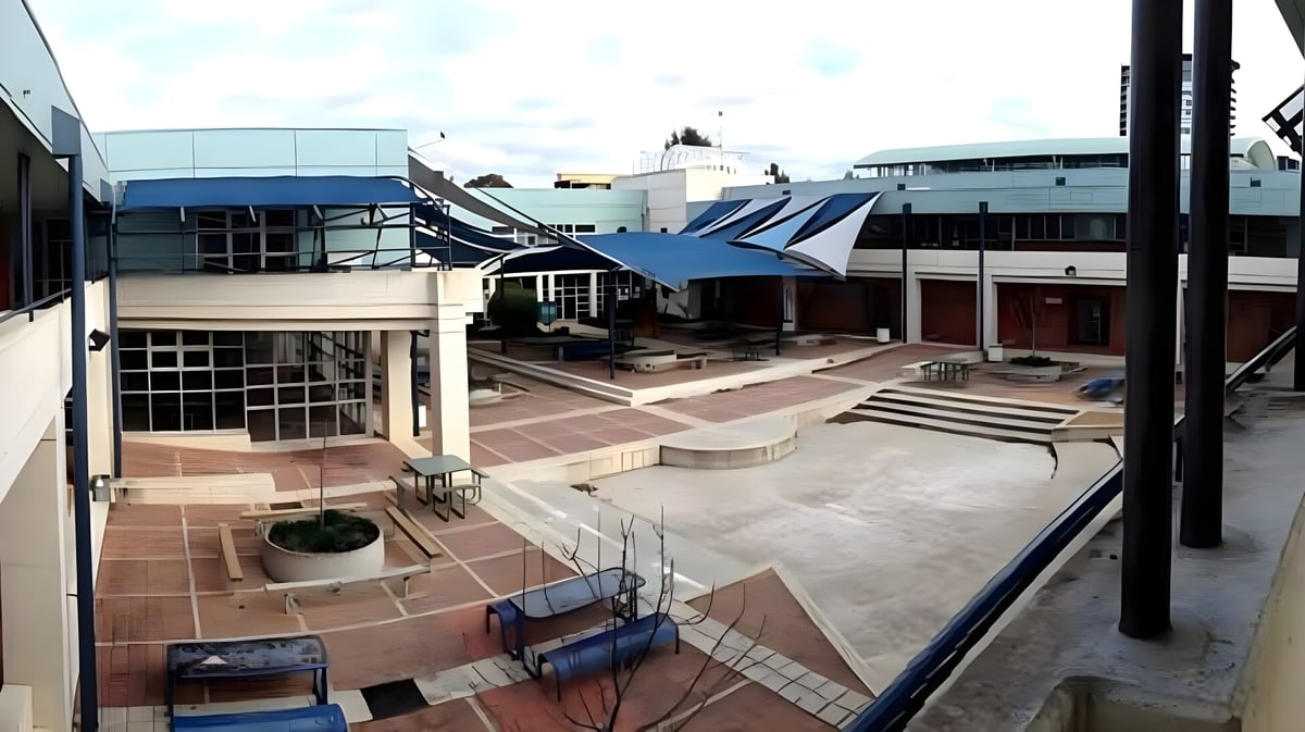 Ein moderner Außenbereich mit Gebäuden und Sitzplätzen auf dem Campus der UC-Lake Ginninderra School vor städtischer Kulisse.