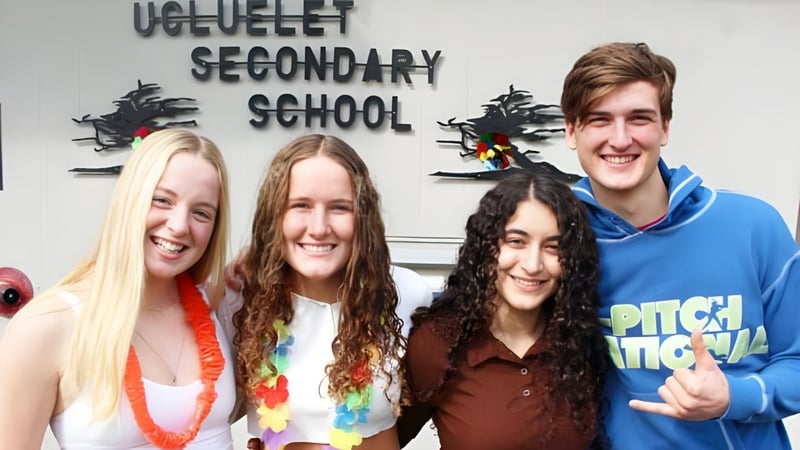 Vier Schülerinnen und Schüler stehen lächelnd vor einem Schild der Ucluelet Secondary School.