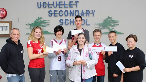 Schüler und Mitarbeiter der Ucluelet Secondary School posieren gemeinsam vor einem Schulgang und zeigen Zertifikate.