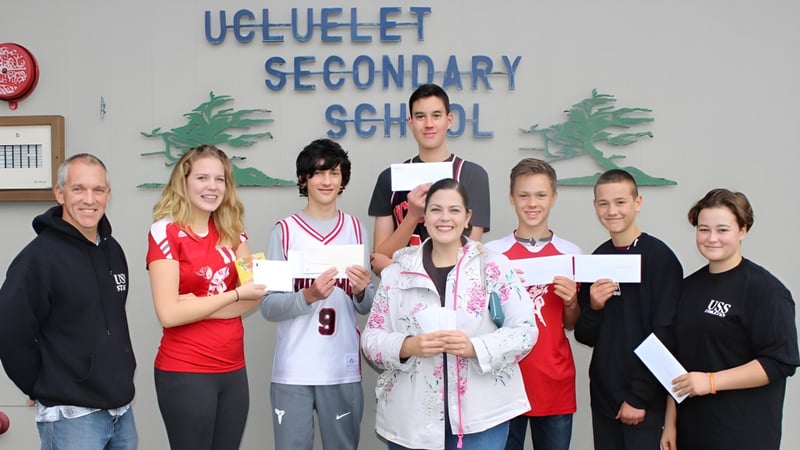 Schüler und Mitarbeiter der Ucluelet Secondary School posieren gemeinsam vor einem Schulgang und zeigen Zertifikate.