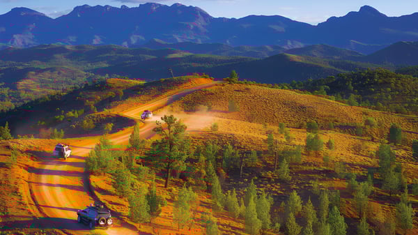 Eine geschwungene Schotterstraße führt durch eine hügelige Landschaft mit bunten Hügeln und mächtigen Bergen in der Ferne nahe der Underdale High School.