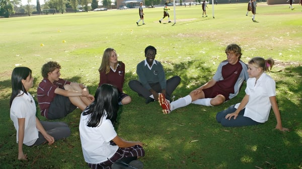 Schüler der Underdale High School sitzen gemeinsam auf einer Wiese in einem parkähnlichen Bereich mit Bäumen im Hintergrund.