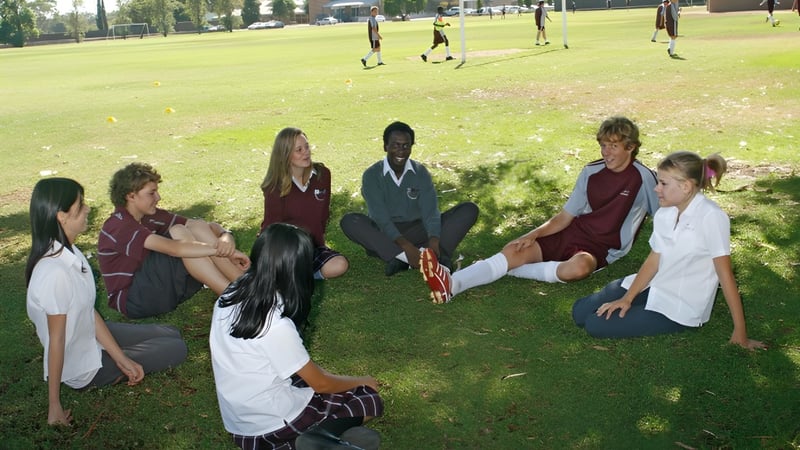 Schüler der Underdale High School sitzen gemeinsam auf einer Wiese in einem parkähnlichen Bereich mit Bäumen im Hintergrund.