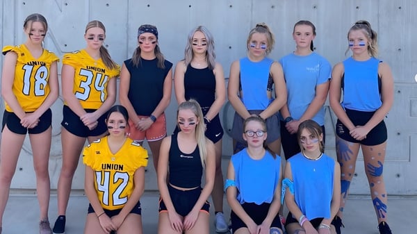 Eine Gruppe junger Sportlerinnen posiert gemeinsam vor einem Holzzaun auf dem Gelände der Union High School.