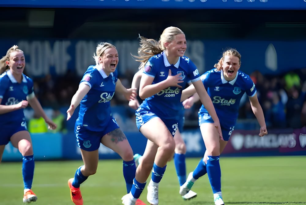 Eine Gruppe weiblicher Fußballspielerinnen der Unisus School läuft gemeinsam auf dem Spielfeld vor einem Stadion.