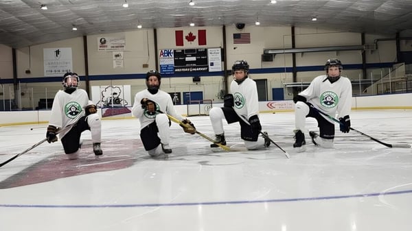 Eine Gruppe von Hockeyspielern in Uniform steht auf dem Eisfeld der Unisus School mit kanadischer und amerikanischer Flagge im Hintergrund.