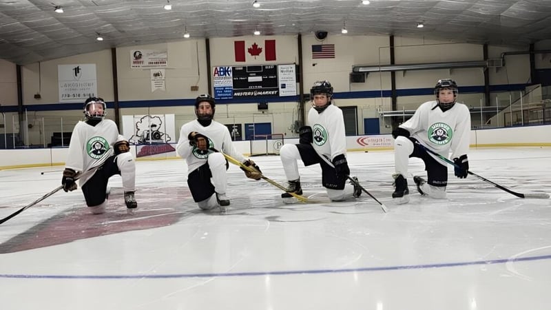 Eine Gruppe von Hockeyspielern in Uniform steht auf dem Eisfeld der Unisus School mit kanadischer und amerikanischer Flagge im Hintergrund.