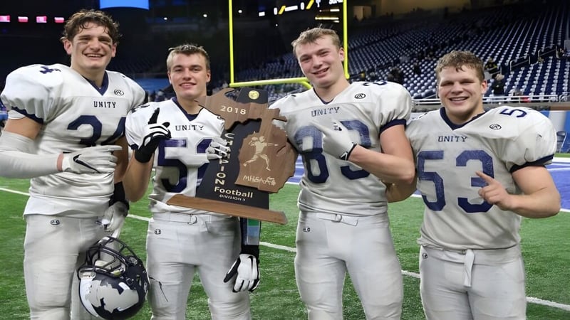 Vier Fußballspieler der Unity Christian High School halten bei Nacht eine Trophäe auf dem Spielfeld.