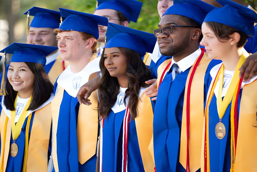Eine Gruppe von Absolventen steht in blauen und gelben Abschlussgewändern auf dem Gelände der Unity Christian High School.