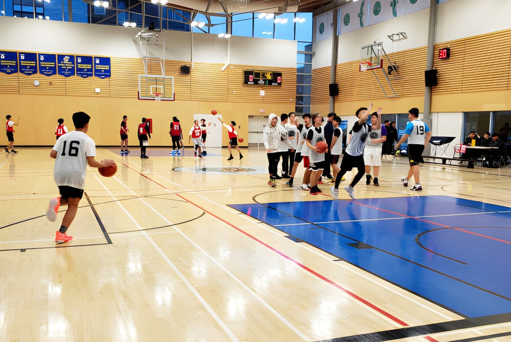 Ein Basketballspiel auf dem Indoor-Court der University Hill Secondary School mit aktiven Schülerinnen und Schülern und Zuschauern im Hintergrund.