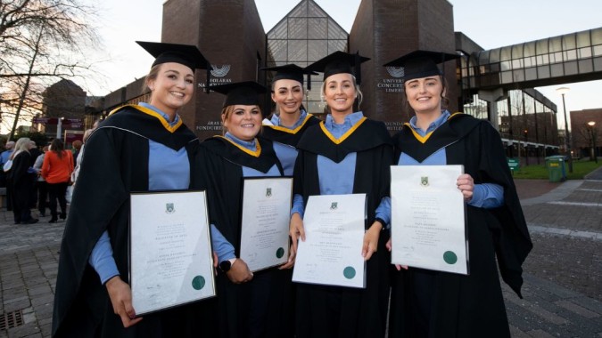 Eine Gruppe Absolventen der University of Limerick steht vor einem modernen Universitätsgebäude und hält ihre Abschlusszeugnisse.