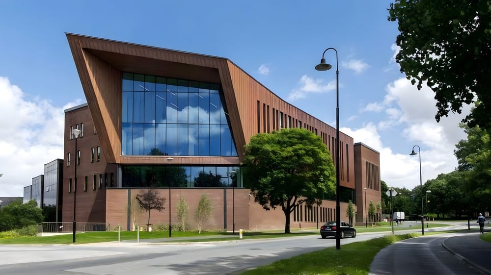 Das moderne Backsteingebäude der University of Limerick mit großen Glasfenstern steht in einer begrünten Umgebung.