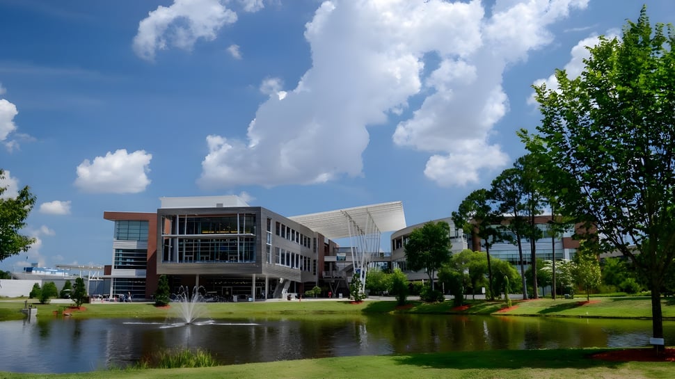 Gebäude mit Glasfassade auf dem Campus der University of North Florida inmitten einer grünen Landschaft mit Teich und Brunnen.