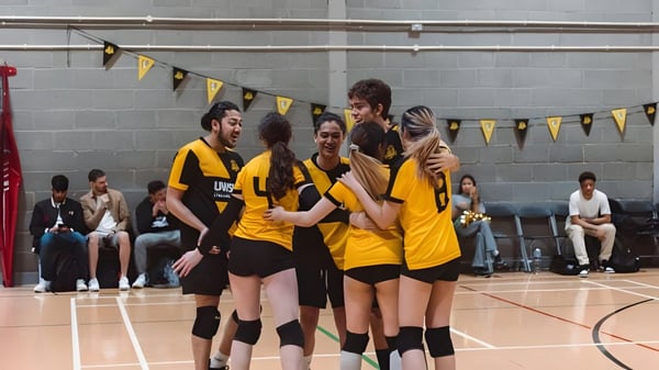 Eine Gruppe von Studierenden der University of Westminster feiert zusammen in einer Sporthalle mit Basketballcourt.