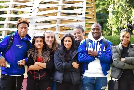 Eine Gruppe Schülerinnen und Schüler steht vor einer Holzstruktur auf dem Campus der University of Westminster.