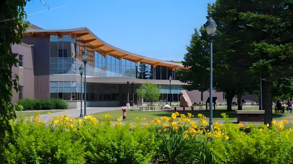 Gebäude der University of Wisconsin-Superior mit Glasfassade und geschwungenem Dach in grüner Landschaft mit gelben Blumen.
