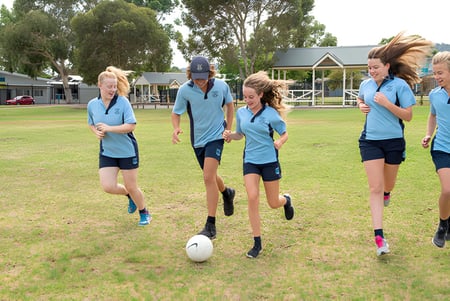 Eine Gruppe junger Athleten der Unley High School läuft gemeinsam über ein grünes Feld mit Schulgebäude im Hintergrund.
