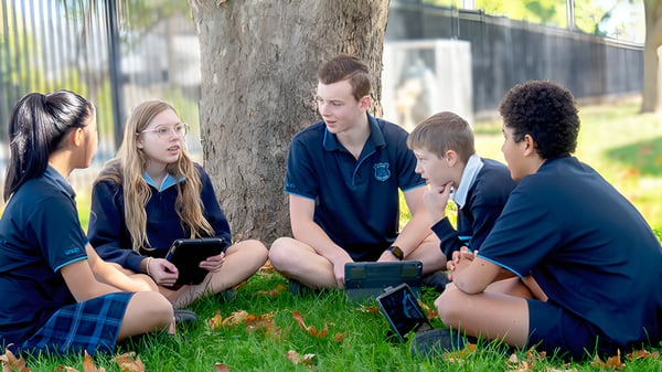 Eine Gruppe Schüler der Unley High School sitzt unter einem Baum und nutzt elektronische Geräte für gemeinsames Lernen.