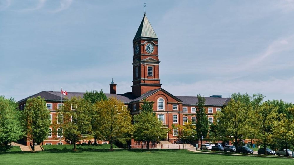 Das Upper Canada College zeigt sein stattliches Backsteingebäude mit hohem Turm in einer parkähnlichen Umgebung mit Bäumen.