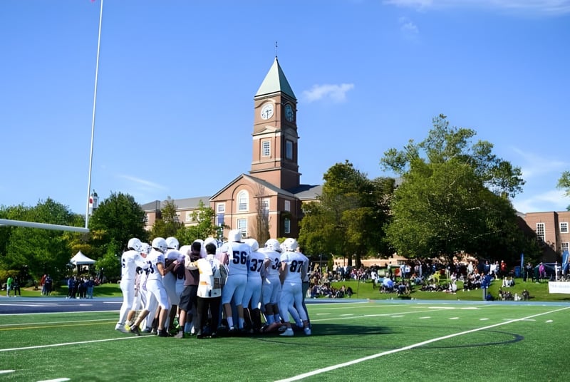 Eine Gruppe von Schülerinnen und Schülern in weißen Uniformen steht auf einer Grasfläche auf dem Gelände des Upper Canada College vor einem hohen Kirchturm.