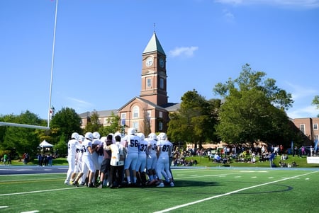 Eine Gruppe von Menschen in weißen Uniformen versammelt sich auf einer Wiese vor dem Kirchturm auf dem Gelände des Upper Canada College.