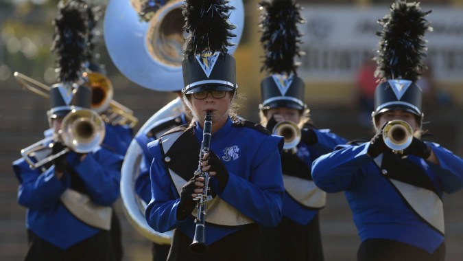 Die Marching Band des Upper Canada College tritt auf einer Bühne in blauen Uniformen mit Federhüten auf.