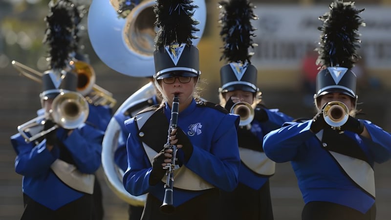 Die Marching Band des Upper Canada College tritt in blauen Uniformen auf einer Bühne vor einem Stadion auf.