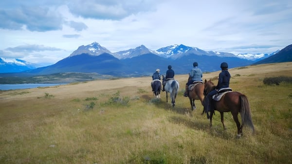 Schüler des Upper Canada College reiten auf Pferden über ein grünes Feld mit schneebedeckten Bergen im Hintergrund.