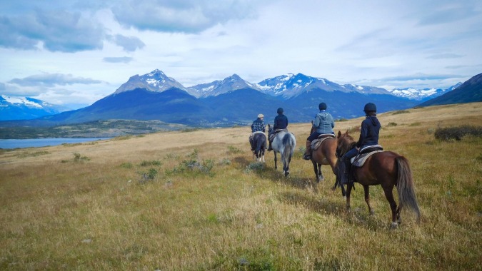 Schüler des Upper Canada College reiten auf Pferden über ein Grasfeld vor schneebedeckten Bergen.