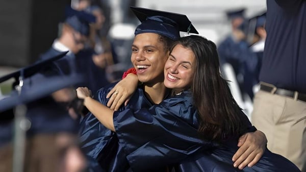Zwei Absolventen in blauen Talaren umarmen sich vor dem Upper Coomera State College während der Abschlussfeier.