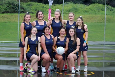 Eine Gruppe junger Athletinnen des Upper Hutt College posiert auf einem Rasenfeld mit Sportplatz und Bäumen im Hintergrund.
