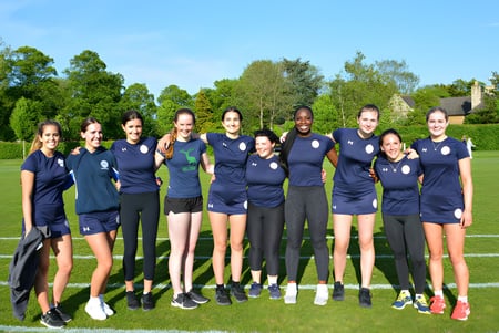Eine Gruppe junger Athletinnen der Uppingham School steht gemeinsam auf einer Wiese unter blauem Himmel.