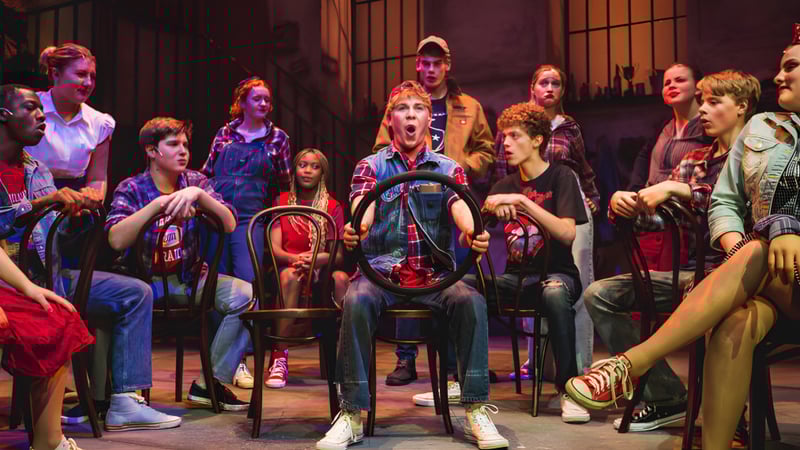 Eine Gruppe von Schülerinnen und Schülern der Uppingham School versammelt sich in einer dunkel beleuchteten Theaterkulisse mit farbiger Bühne im Hintergrund.