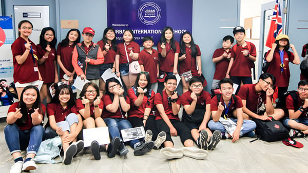 Eine Gruppe Schüler in roten Uniformen posiert vor einem AIESEC International Hintergrund auf dem Campus der Urban International High School.