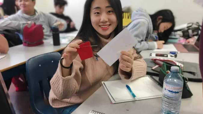 Eine Schülerin der Urban International High School sitzt lächelnd am Tisch und hält eine rote Karte in der Hand.