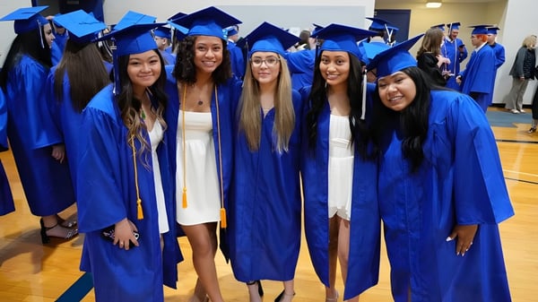 Eine Gruppe junger Frauen in blauen Abschlussroben steht zusammen auf dem Campus der Urbandale Community School District.