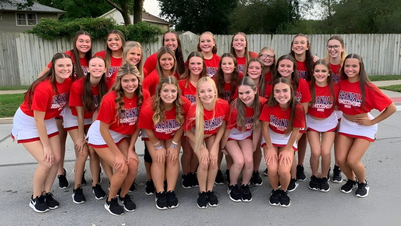 Eine Gruppe Schülerinnen in roten Uniformen steht draußen vor einem Holzzaun auf dem Campus der Urbandale Community School District.