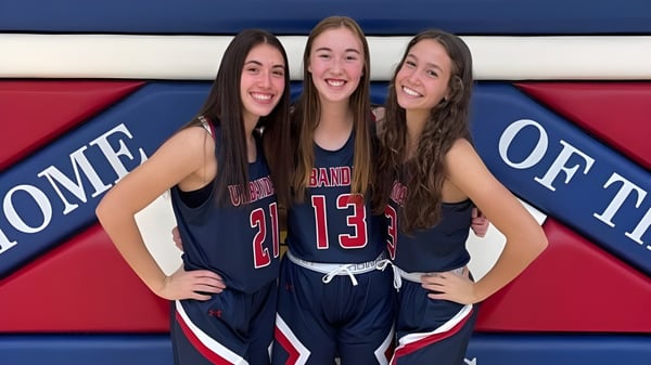 Drei Schülerinnen der Urbandale High School in Sportuniformen posieren gemeinsam vor einem bunten Hintergrund.