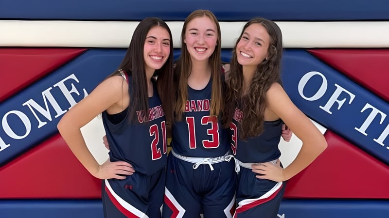 Drei Schülerinnen der Urbandale High School in Sportuniformen posieren gemeinsam vor einem bunten Hintergrund.