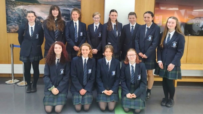 Eine Gruppe Schüler im Ursuline College Sligo steht zusammen in einem Klassenzimmer vor einem Landschaftsgemälde.