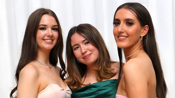 Drei Schülerinnen des Ursuline College Sligo posieren gemeinsam vor einem weißen Hintergrund in formeller Kleidung.