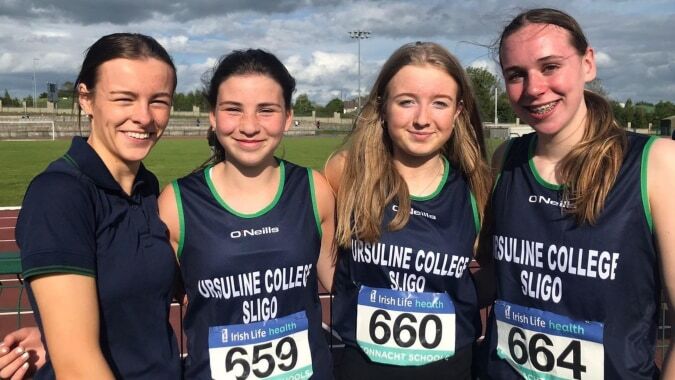 Vier Schülerinnen des Ursuline College Sligo stehen gemeinsam auf dem Sportfeld bei bewölktem Himmel.