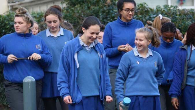 Eine Gruppe von Schülerinnen und Schülern der Ursuline Secondary School in blauen Schuluniformen geht gemeinsam über den Campus mit Grünflächen im Hintergrund.