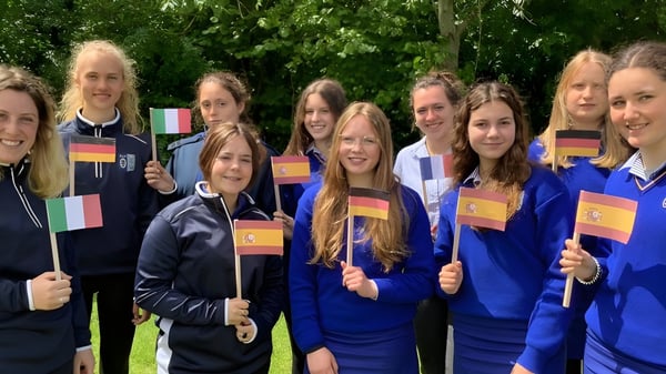 Schülerinnen der Ursuline Secondary School (Cork) stehen draußen in blauen Uniformen und halten verschiedene Länderflaggen.
