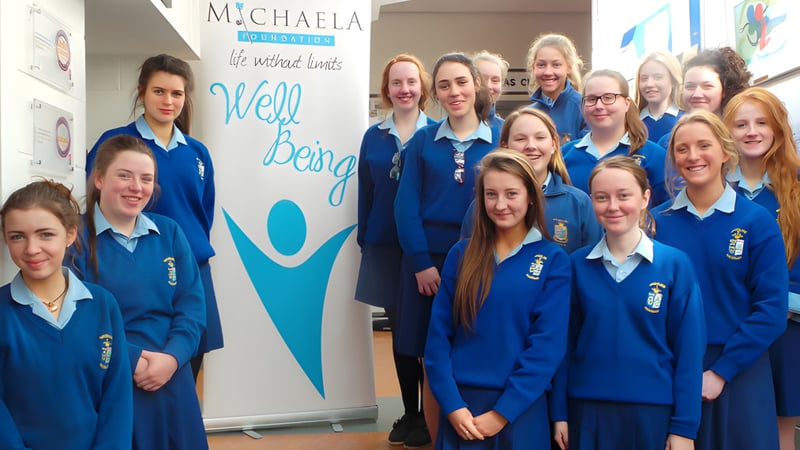 Schüler der Ursuline Secondary School Thurles stehen vor einer Wand mit dem Schriftzug 'Michaela' und 'Well being'.